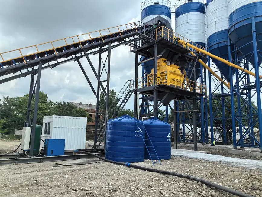 Elevated central mixer beneath aggregate conveyor beside silos
