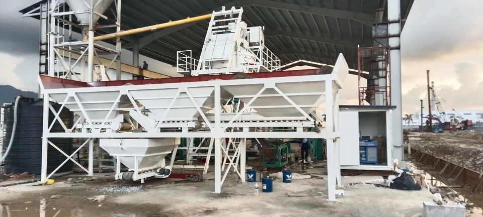 Concrete batching equipment under a roof with aggregate bins and an adjacent silo
